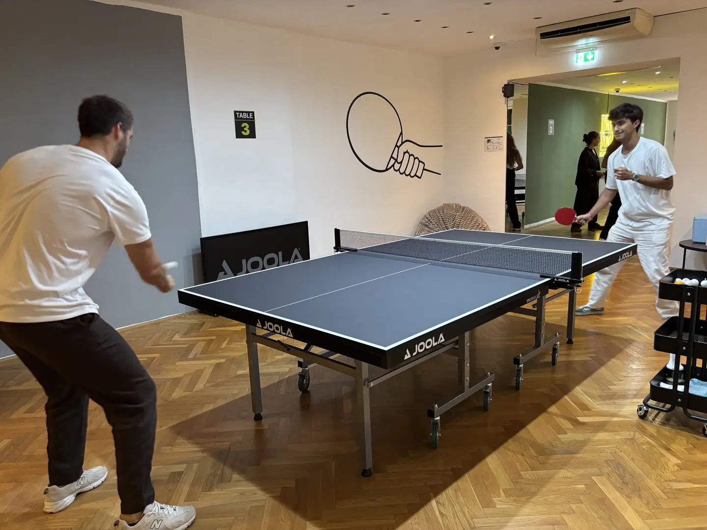 Ballwechsel an Tisch 3, im Hintergrund weitere Gäste beim Tischtennis