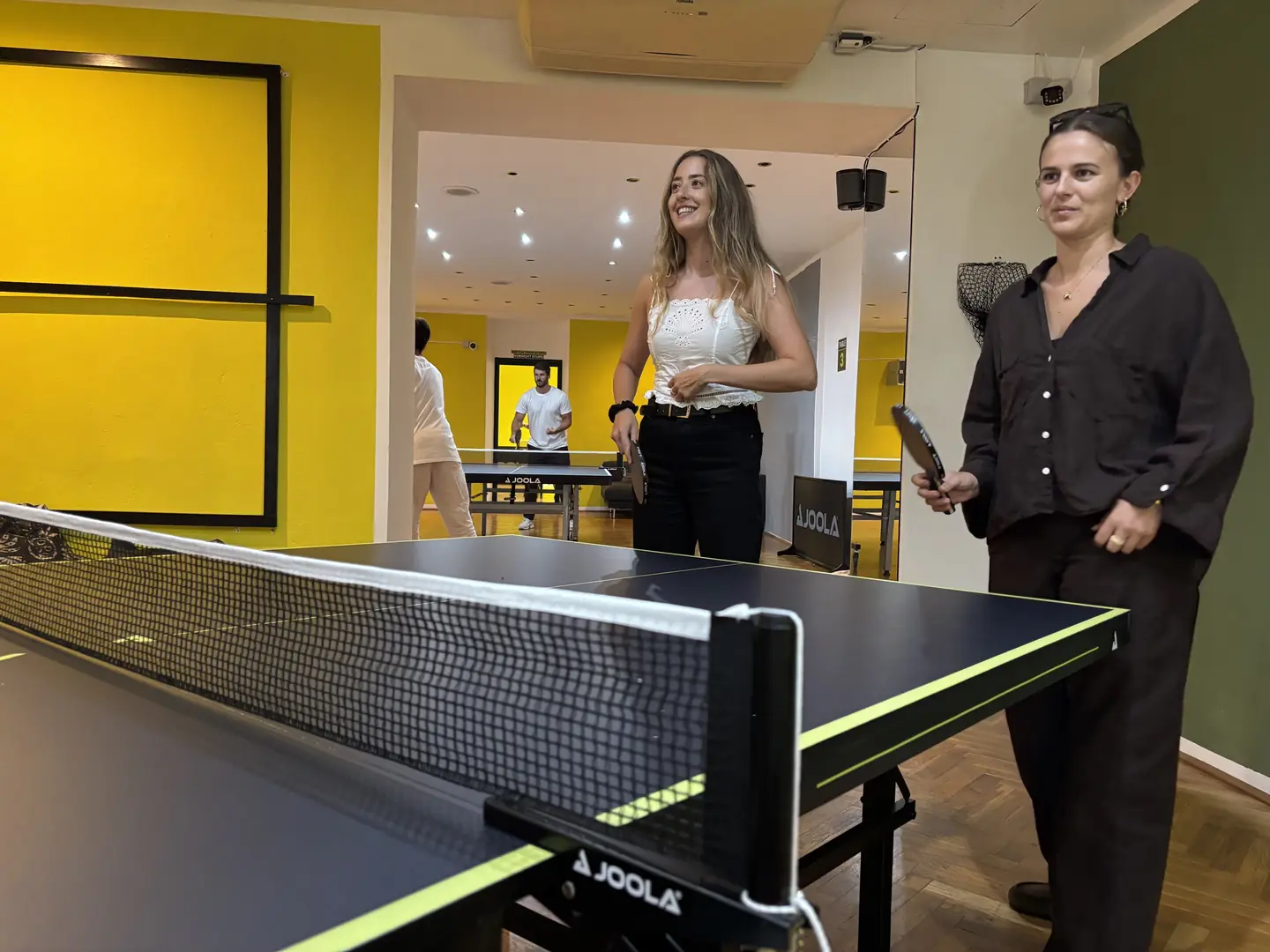 Zwei Spielerinnen mit Schlägern vor der gelben Wand im Ping Pong Garden Salzburg