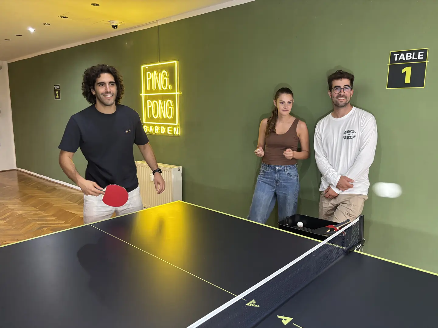 Drei Spielende an Tisch 1 unter dem Ping-Pong-Garden-Neonschild in Salzburg